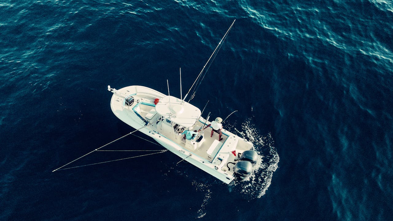 Aerial shot of a fishing boat in the deep blue ocean with a person onboard.