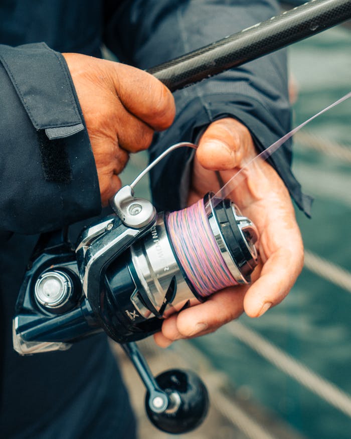 Detailed view of hands managing a fishing reel outdoors, perfect for fishing enthusiasts.
